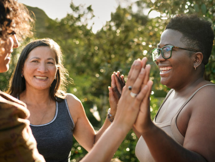 a group of women high-fiving outside with greenery 